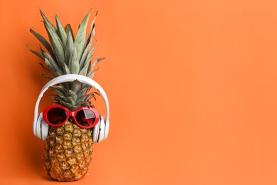 Photo of Pineapple with sunglasses and headphones on orange background, space for text. Creative concept