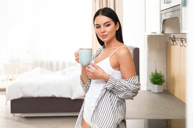 Beautiful young woman in white underwear drinking coffee at home