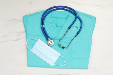 Photo of Medical uniform, stethoscope and protective mask on white marble table, flat lay