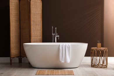Modern ceramic bathtub and folding screen near brown wall in room