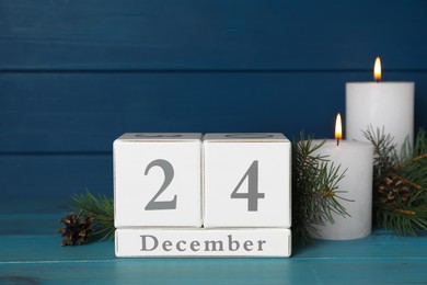 Christmas Eve - December 24. Block calendar, burning candles and fir tree branches on light blue wooden table