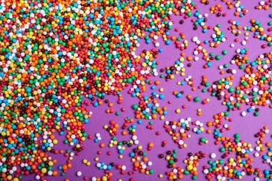 Colorful sprinkles on purple background, flat lay. Confectionery decor