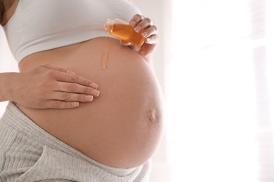 Young pregnant woman with cosmetic product indoors, closeup. Space for text