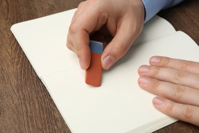 Man erasing something in notebook at wooden table, closeup