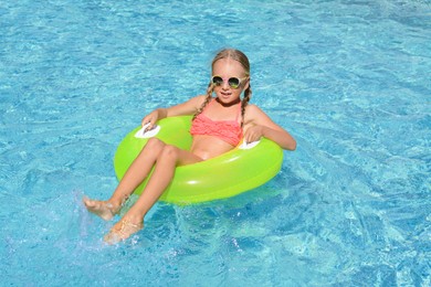 Cute little girl with inflatable ring in pool on sunny day