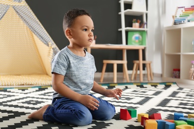 Cute little African-American child playing with building blocks on floor in kindergarten. Indoor activity