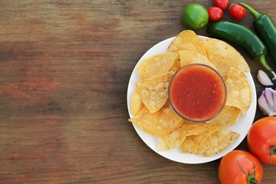 Photo of Tasty salsa sauce with tortilla chips and ingredients on wooden table, flat lay. Space for text