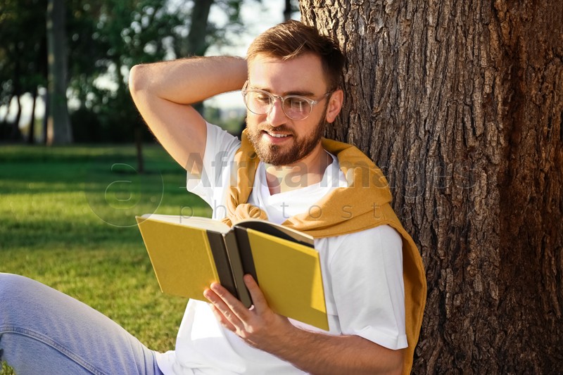 Young man reading book near tree in park