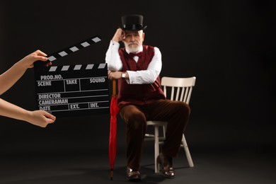 Photo of Senior actor performing role while second assistant camera holding clapperboard on black background, selective focus. Film industry