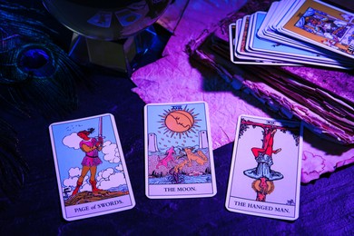 Page of Swords, Hanged Man and Moon tarot cards on dark table, color toned