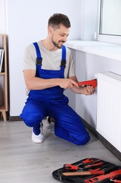 Professional plumber using adjustable wrench for installing new heating radiator in room