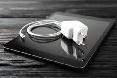 Photo of Tablet and charging cable with adapter on black wooden table