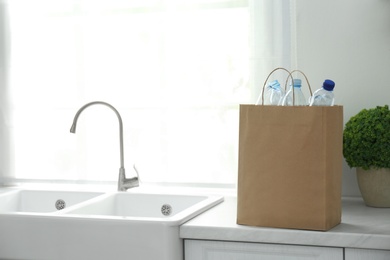 Paper bag with used plastic bottles on kitchen counter, space for text. Recycling problem