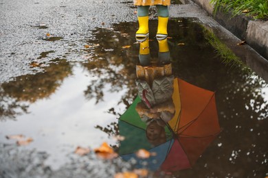 Photo of Little girl wearing yellow rubber boots standing in puddle outdoors, space for text
