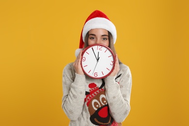 Woman in Santa hat with clock on yellow background. New Year countdown