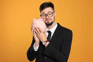 Happy businessman with piggy bank on orange background