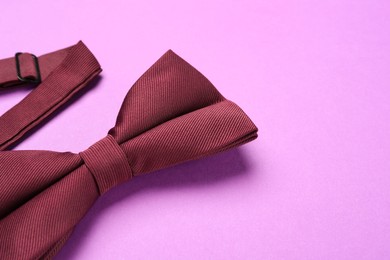 Stylish burgundy bow tie on violet background, closeup. Space for text
