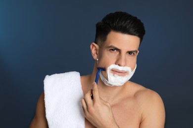Handsome man shaving with razor on blue background