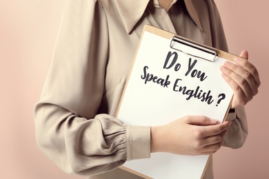 Woman holding clipboard with question Do You Speak English on pink background, closeup