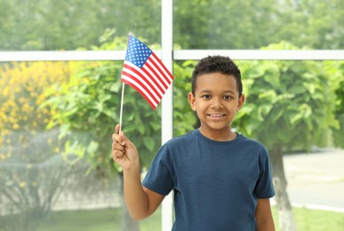Happy African-American boy holding national flag near window indoors