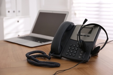 Stationary phone and headset on wooden table indoors. Hotline service