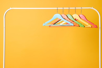 Photo of Bright clothes hangers on metal rack against yellow background