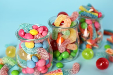 Jars with different delicious candies on light blue background
