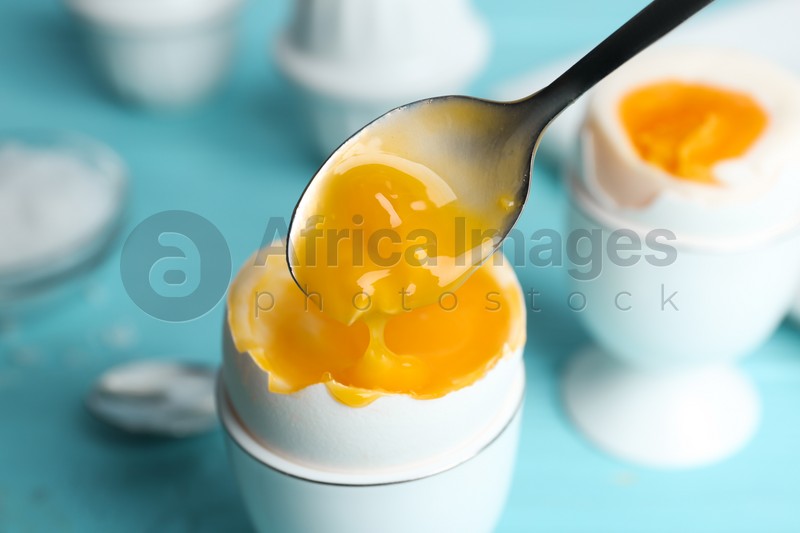 Eating soft boiled chicken egg with spoon at light blue table, closeup