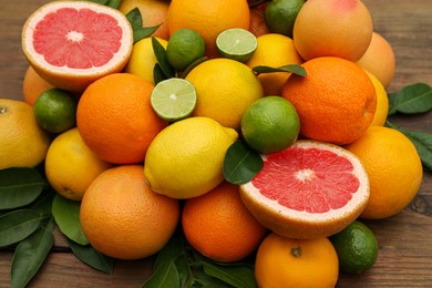 Photo of Different citrus fruits with green leaves on wooden table, closeup