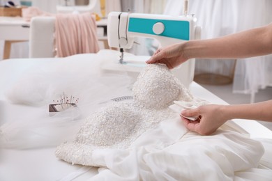 Dressmaker creating beautiful wedding dress with embroidered bustline and bow at table in workshop, closeup