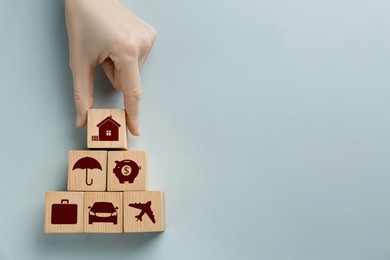 Woman building pyramid of wooden cubes with different icons on light background, top view. Insurance concept