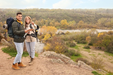 Couple of travelers with backpacks and map enjoying beautiful view near mountain river. Autumn vacation