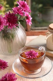 Beautiful chrysanthemum flowers and cup of tea on beige textured table near window. Autumn still life