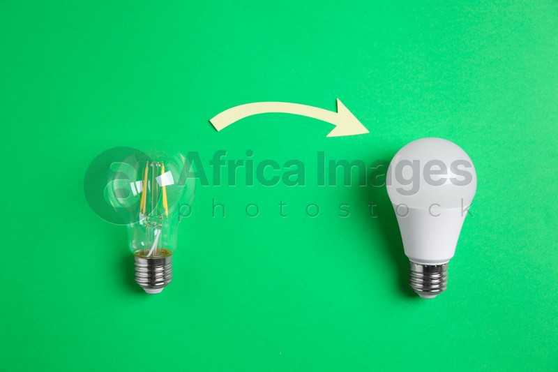 LED and simple light bulbs with arrow on green background, flat lay. Energy saving concept