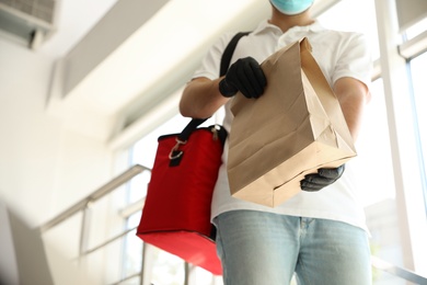 Courier in protective mask and gloves with order indoors, closeup. Restaurant delivery service during coronavirus quarantine