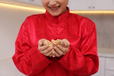 Photo of Young woman holding bowl of tasty fortune cookies with predictions in kitchen, closeup