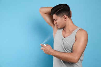 Photo of Handsome man applying deodorant to armpit on turquoise background, space for text
