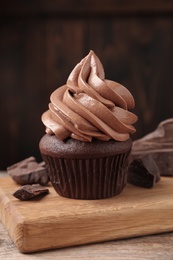 Delicious cupcake with cream and chocolate pieces on wooden table, closeup