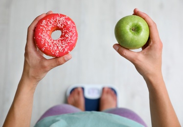 Choice concept. Top view of woman with apple and doughnut standing on scales, closeup