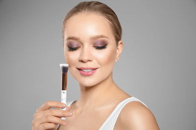 Beautiful woman applying makeup with brush on light grey background