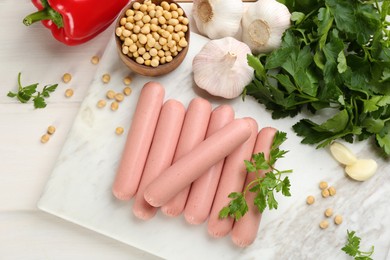 Fresh raw vegetarian sausages and vegetables on white wooden table, flat lay