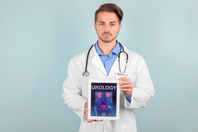 Male doctor holding tablet with urinary system on screen against color background