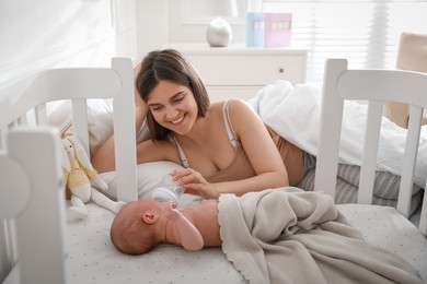 Happy young mother feeding her newborn baby from bottle at home