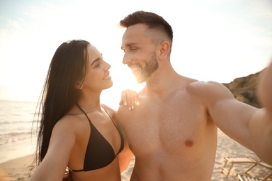 Happy young couple taking selfie on beach at sunset