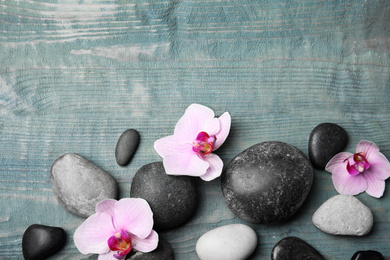 Stones with orchid flowers and space for text on blue wooden background, flat lay. Zen lifestyle