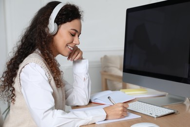 African American woman with headphones using modern computer for studying at home. Distance learning