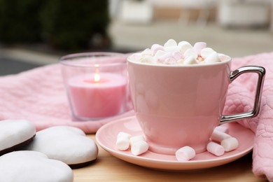 Photo of Cup of tasty cocoa with marshmallows, pink sweater, cookies and burning candle on wooden table outdoors