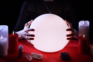 Soothsayer using glowing crystal ball to predict future  at table in darkness, closeup. Fortune telling