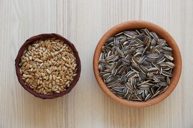 Bowls with organic sunflower seeds on white wooden table, flat lay