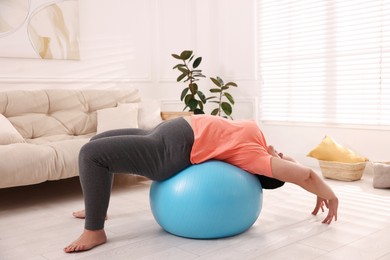 Overweight mature woman doing exercise with fitness ball at home